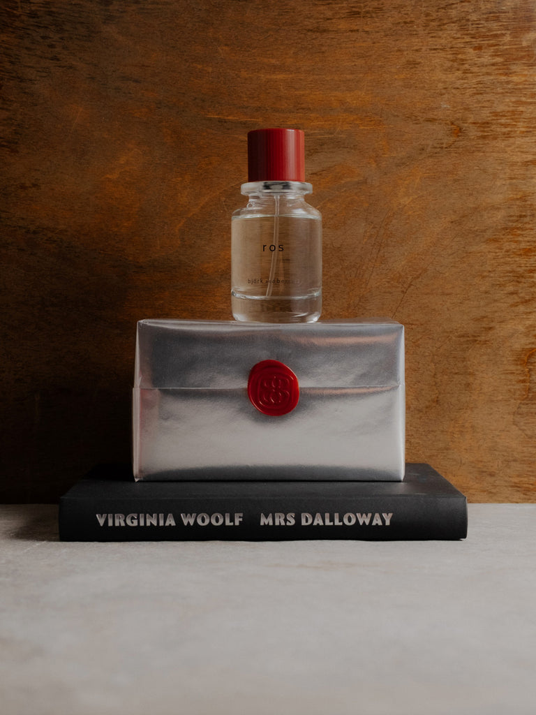 Ros edp bottle on a silver wrapped perfume box with a red seal, placed on top of a book titled 'Mrs Dalloway'.