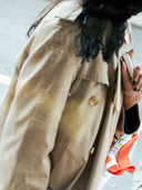 A faceless woman wearing a beige coat, holding a Björk and berries travel bottle to her chest. 