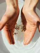 Hands in a tub of water, holding Björk and Berries Bathsalt. 
