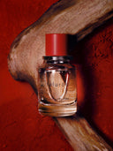 A bottle of Björk and Berries Faluröd Eau de Perfume lying down, and reasting on pice of cedar wood, with a red clay background. 