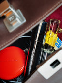 An open purse disclosing what's in the bag. Among different sorts of items you can se a björk and berries travel bottle as well as a white forest travel sized eau de perfume. 