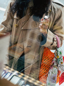 A woman in beige coat locking into a book store and holding a björk and berries travel bottle. 