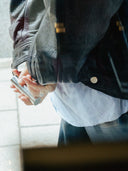 A person wearing a lather jacket holding a björk and berries travel bottle with both hands behind his back. 