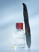 Vanilla bean leaning on a bottle of Björk and Berries vanilla veil eau de perfume. against a fogy blue and white background. 